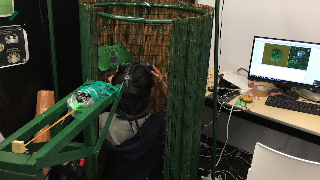 簾を円形にし竹筒に見立てた中央に男性が正座している画像。男性は VR ゴーグルを被っている